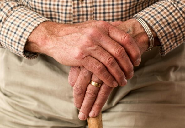A detailed image of elderly hands clasping a wooden cane, symbolizing aging and support.