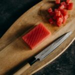 Close-up of fresh tuna cubes and knife on a wooden chopping board, perfect for Asian cuisine preparation.