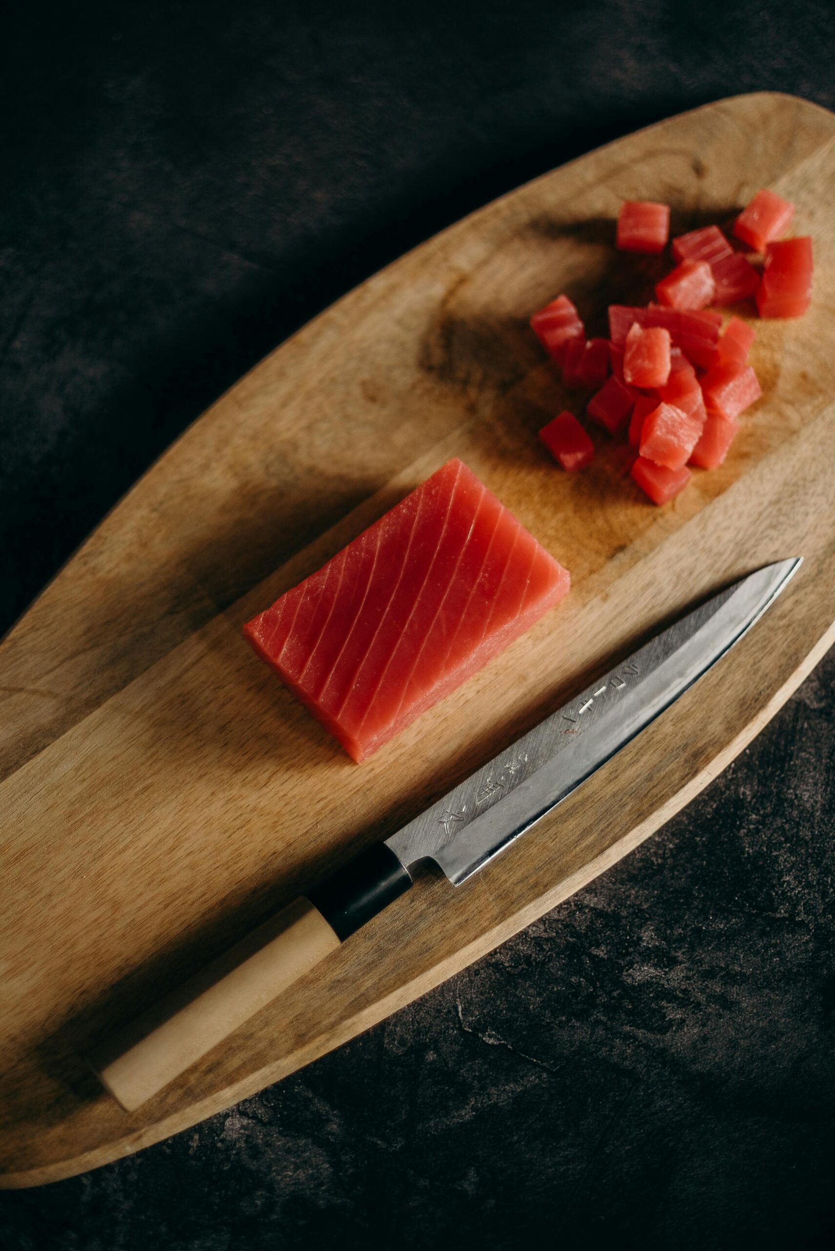 Close-up of fresh tuna cubes and knife on a wooden chopping board, perfect for Asian cuisine preparation.