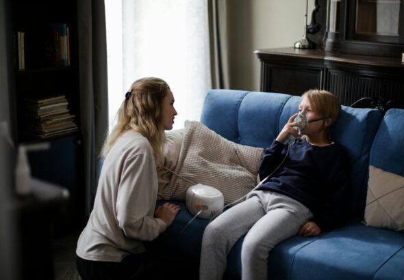 A mother assists her sick child using a nebulizer at home, providing comfort and care.