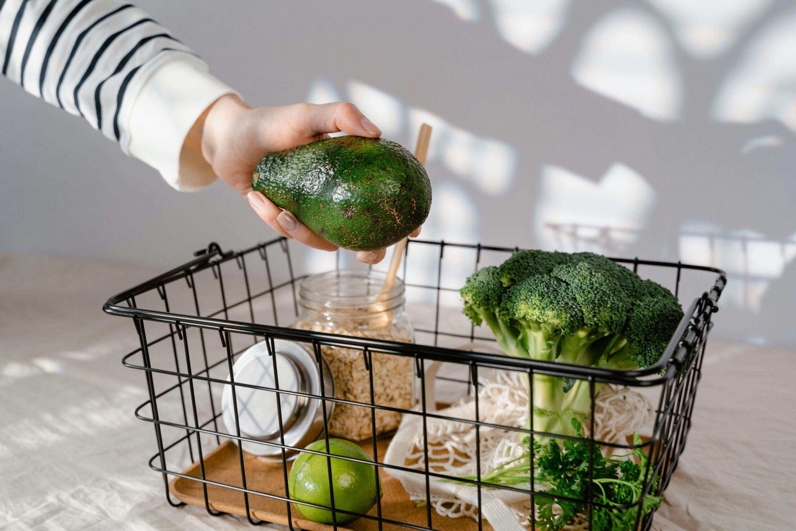 Fresh groceries basket with avocado, broccoli, oats, and lime for healthy living.