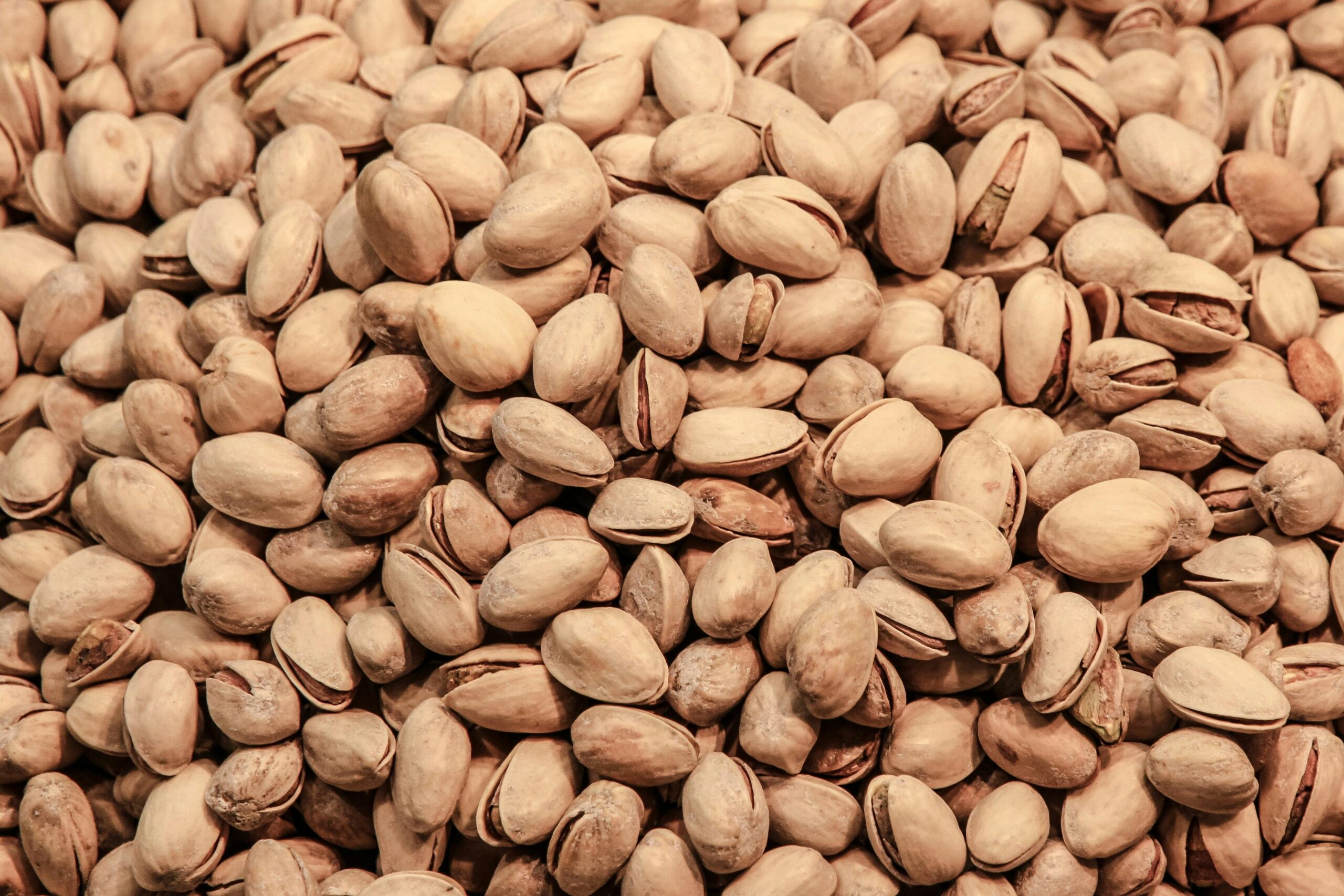 A detailed close-up image of pistachio nuts, showcasing their natural texture and earthy tones.